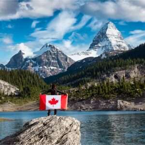 Person holding Canadian flag in mountainous landscape